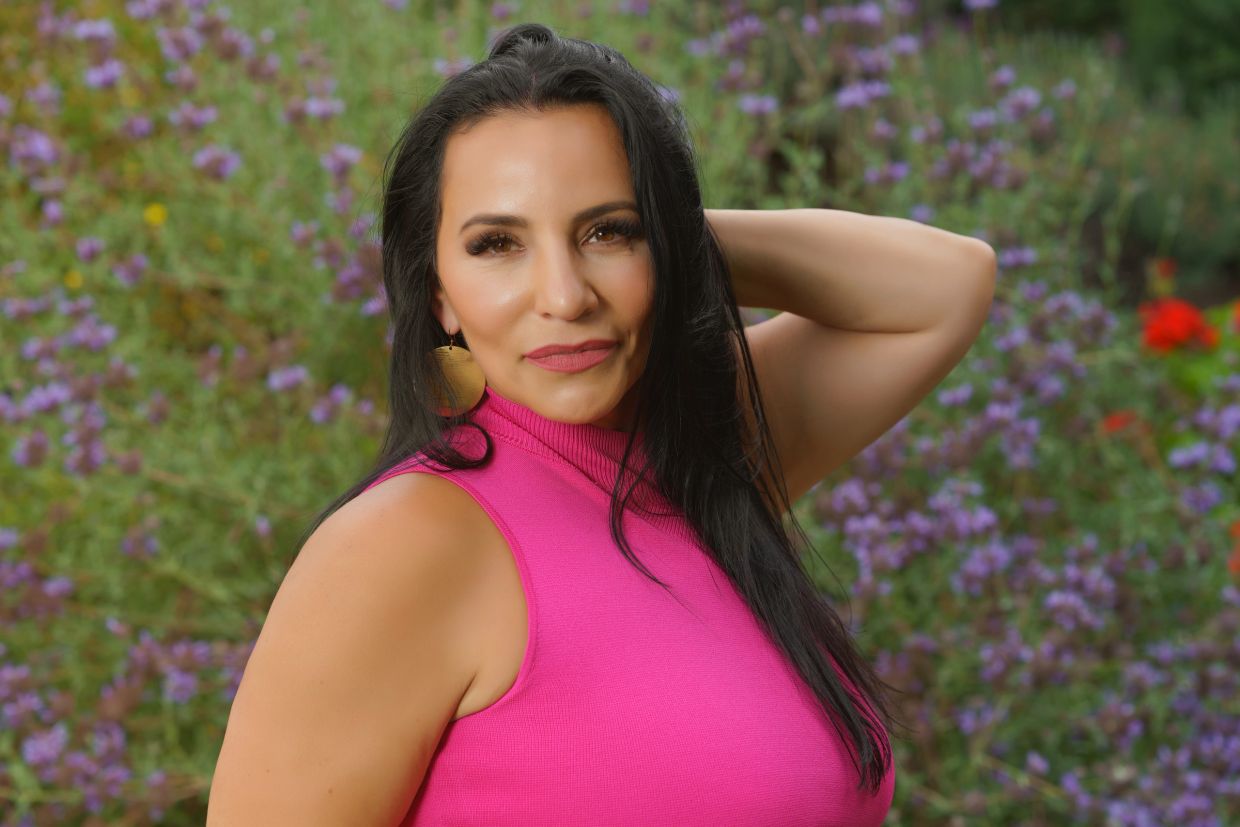 Woman in pink sleeveless top posing outdoors with flowers.