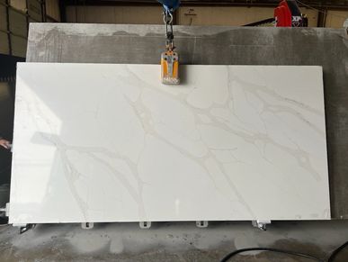 A large white marble slab with beige veining being lifted by a clamp.