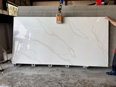 Large white marble slab with subtle gray veining being held upright by a person and a clamp.