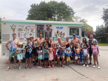 A large group of people posing happily in front of an ice cream truck on a sunny day.