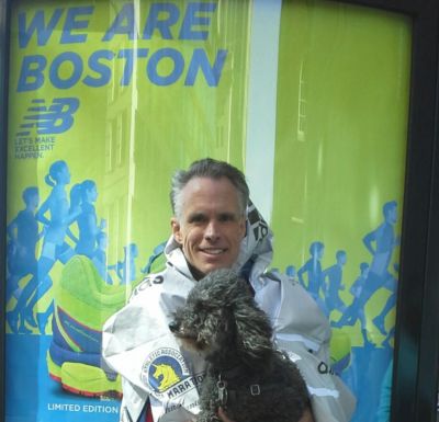 Man with dog in front of a Boston marathon poster.