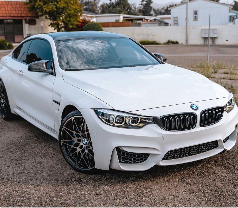 White BMW M4 parked on a gravel surface with a sleek design.