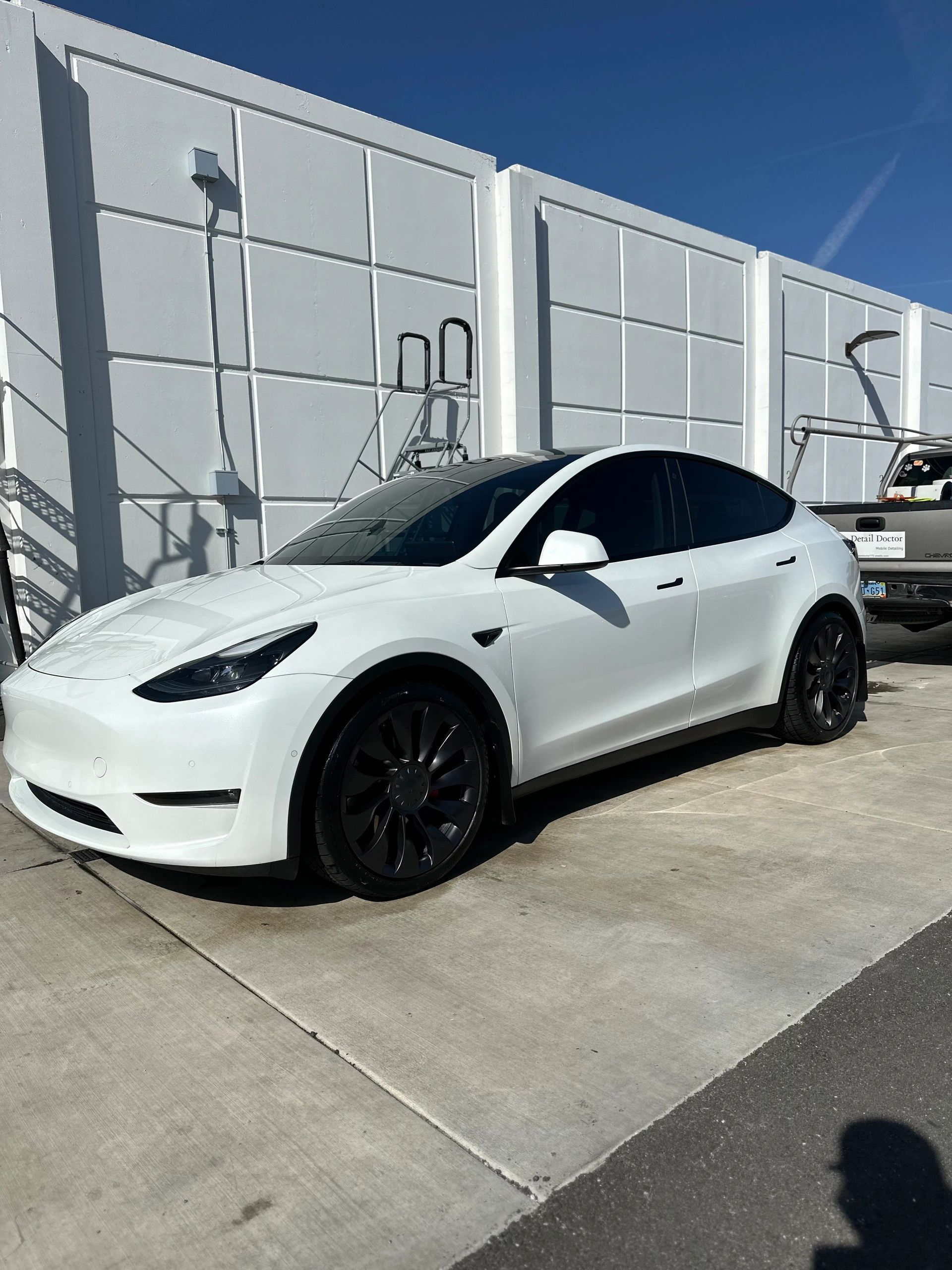 White Tesla parked in front of a modern white wall under clear blue sky.