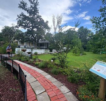 Curved brick pathway leads to a charming house surrounded by lush garden and trees.
