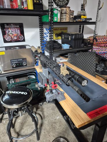 A rifle mounted on a workbench in a workshop with various tools and items.