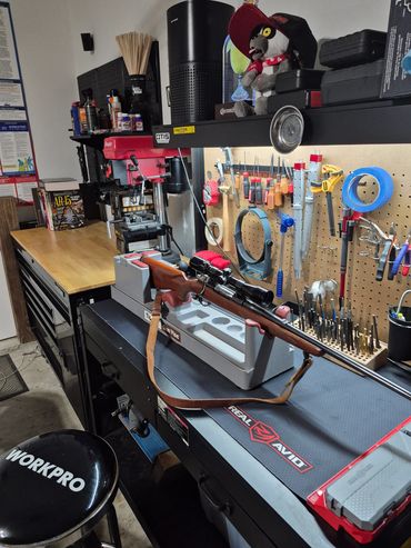 A well-organized gun cleaning and maintenance workspace with tools, a rifle in a vise, and reference books.