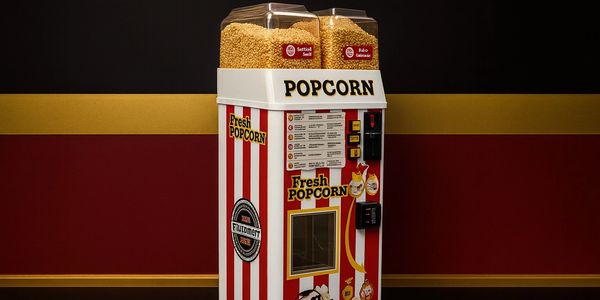 A vintage popcorn machine with red and white stripes and large bins of popcorn kernels.