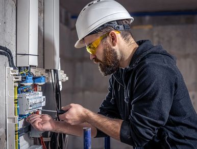 A male electrician works in a switchboard with an electrical connecting cable.