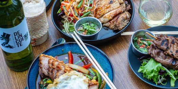 A table set with various Asian-inspired dishes and drinks including grilled meats and a fried egg.