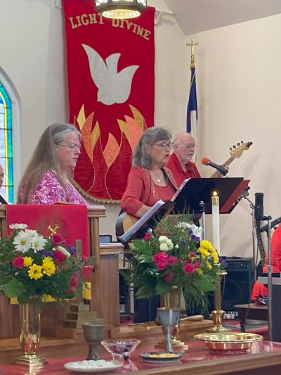 Three musicians performing in a church with floral arrangements and banners.