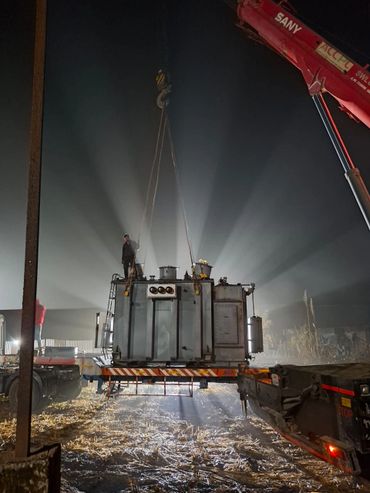 A large industrial machine being lifted by a crane at night.