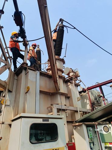 Two workers in safety helmets perform maintenance on industrial equipment outdoors.