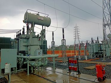 An electrical substation with transformers and safety equipment under a cloudy sky.