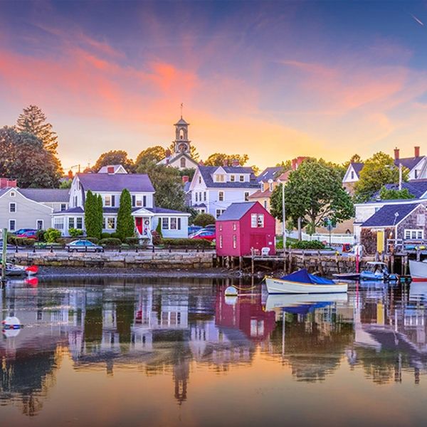Colorful coastal town at sunset with boats and calm water reflections.