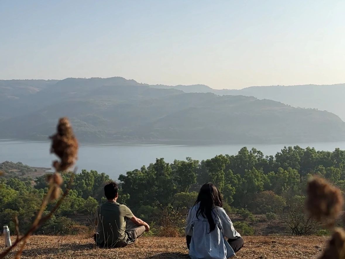 Two people sitting and admiring a scenic lake view with distant hills.