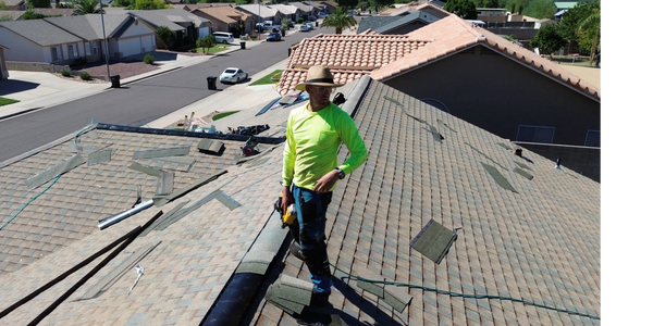 Roofer in a bright yellow shirt working on a residential roof under clear skies.