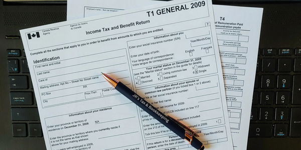 A Pen on top of a Tax Return and T4 on a Laptop
