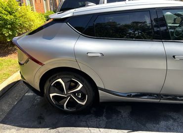 Silver Kia electric SUV parked on a street near greenery.