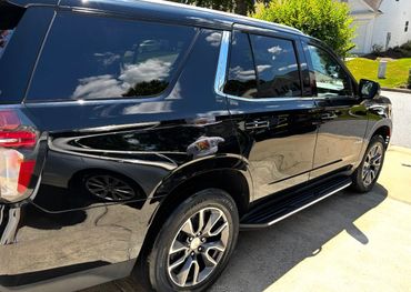 A shiny black Chevrolet Tahoe parked on a driveway under sunlight.
