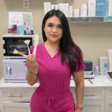 Woman in pink scrubs holding skincare tools in a clinic.