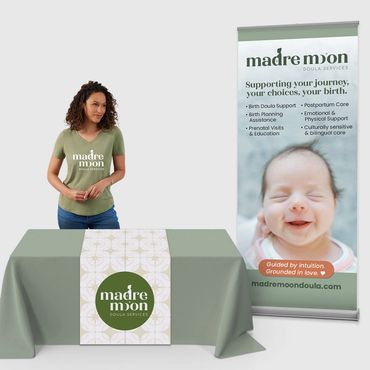 Table with Madre Moon table drape, woman in branded t-shirt, and bannerstand.