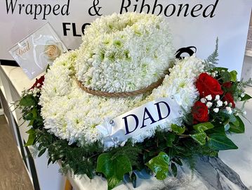 Floral tribute hat with 'DAD' ribbon and red roses for remembrance.