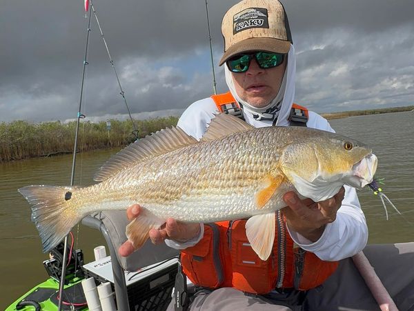 Fisherman proudly holding a large fish on a boat under cloudy skies.
