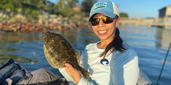 Woman proudly holding a flatfish while fishing on a sunny day.