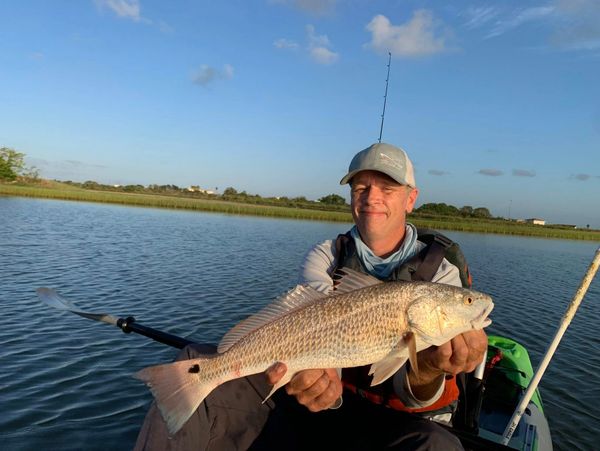 Man holding a large fish on a boat in calm water during daytime.
