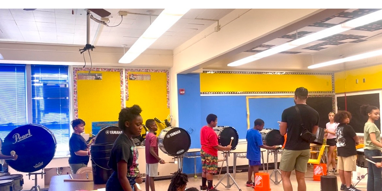 Children practicing drums in a colorful classroom with an instructor.