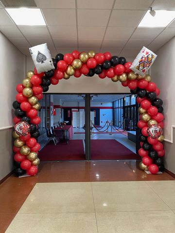 A festive balloon arch with playing card decorations in red, black, and gold colors.