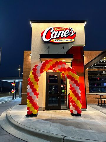 Raising Cane's restaurant entrance decorated with balloon arch at night.