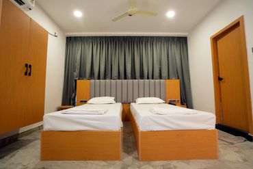 Minimalist twin beds in a clean, modern room with wooden furniture and gray curtains.