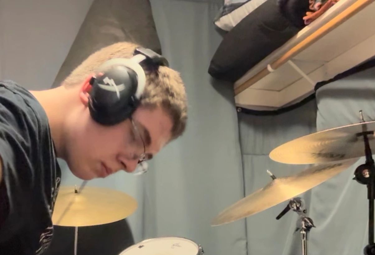Young man with headphones playing a drum set indoors.