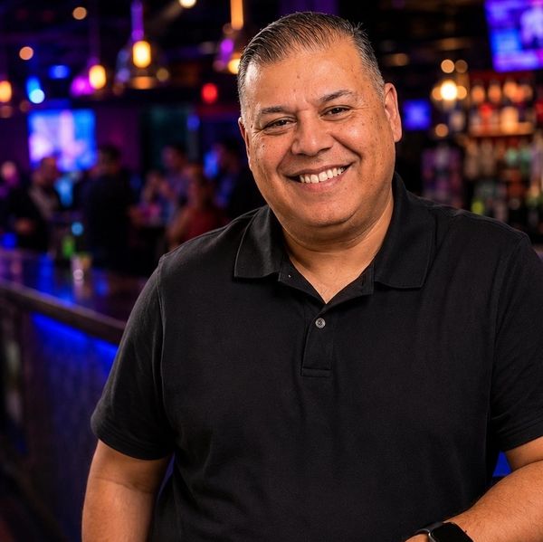 Smiling man in black polo shirt at a bar.