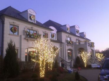 A large house decorated with Christmas wreaths and lights on trees at dusk.