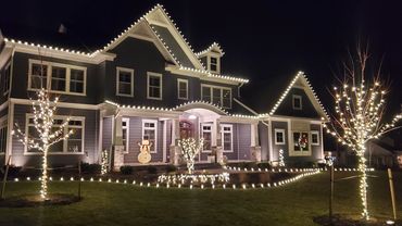 A house decorated with white Christmas lights and a wooden snowman at night.