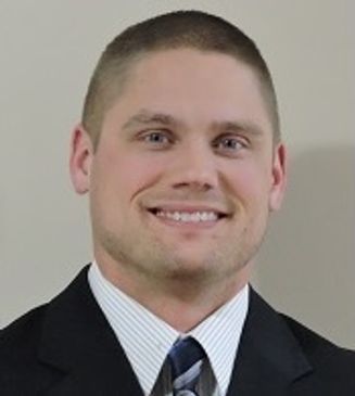 Smiling man in a suit and tie against a plain background.