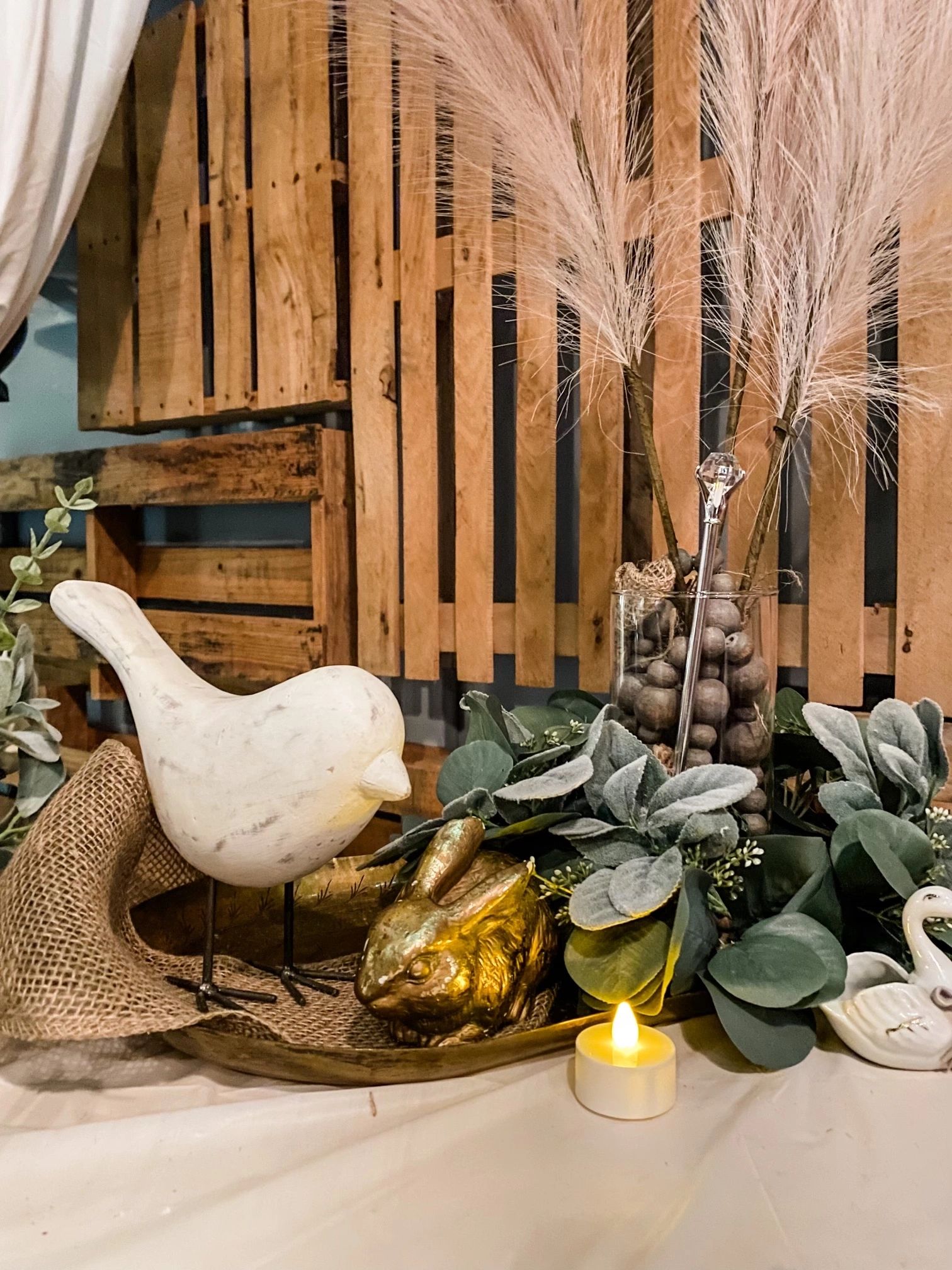 ceramic bird and wooden pallets used for wedding decor on a table with a candle