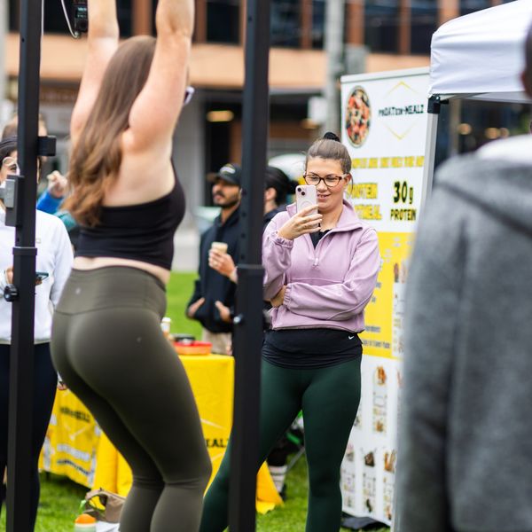 Woman hanging from her arms on a pull up bar while her friend takes photos with her cellphone