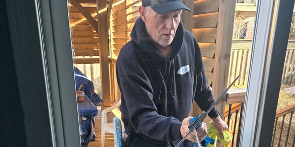 Man cleaning a glass sliding door with a squeegee outdoors.