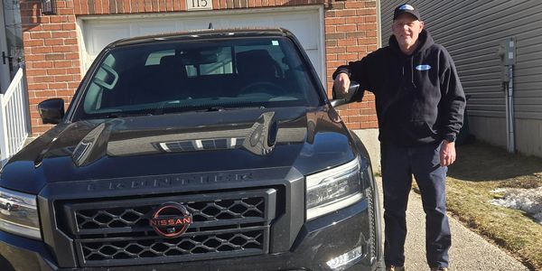 Man standing next to a black Nissan truck with a custom license plate.