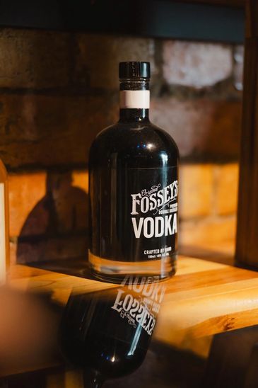 A bottle of Fossey's Vodka on a wooden shelf with its reflection below.