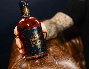 Hand holding a bottle of Fossey's Single Malt Whisky on a leather surface.
