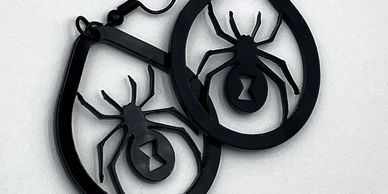 Black spider-shaped earrings with teardrop frames on a white background.