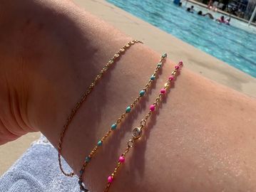 Three delicate anklets on a sunlit leg by a pool.