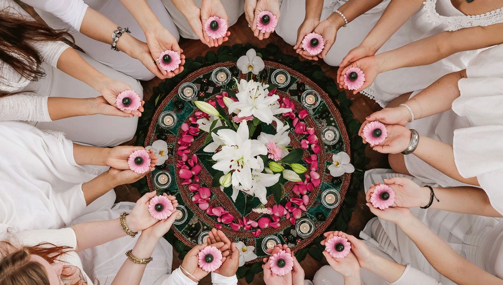 People in white holding pink flowers around a decorated floral mandala.