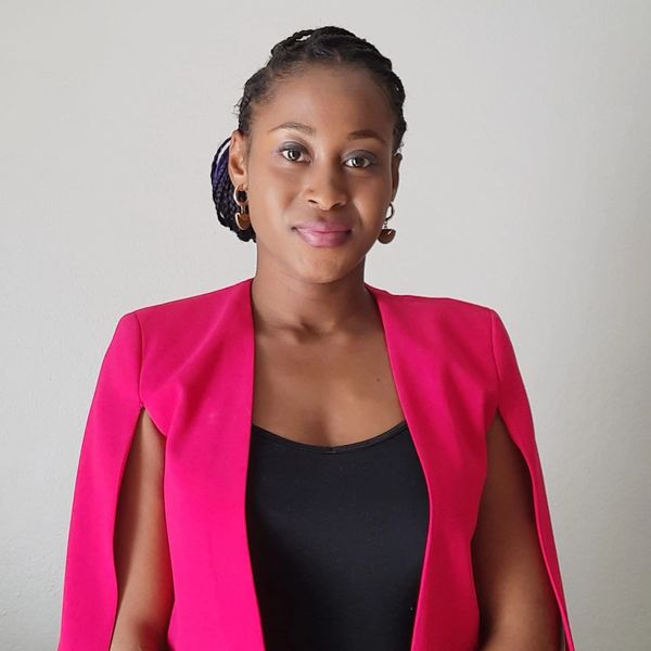 Confident woman in a bright pink blazer and black top, posing against a plain background.