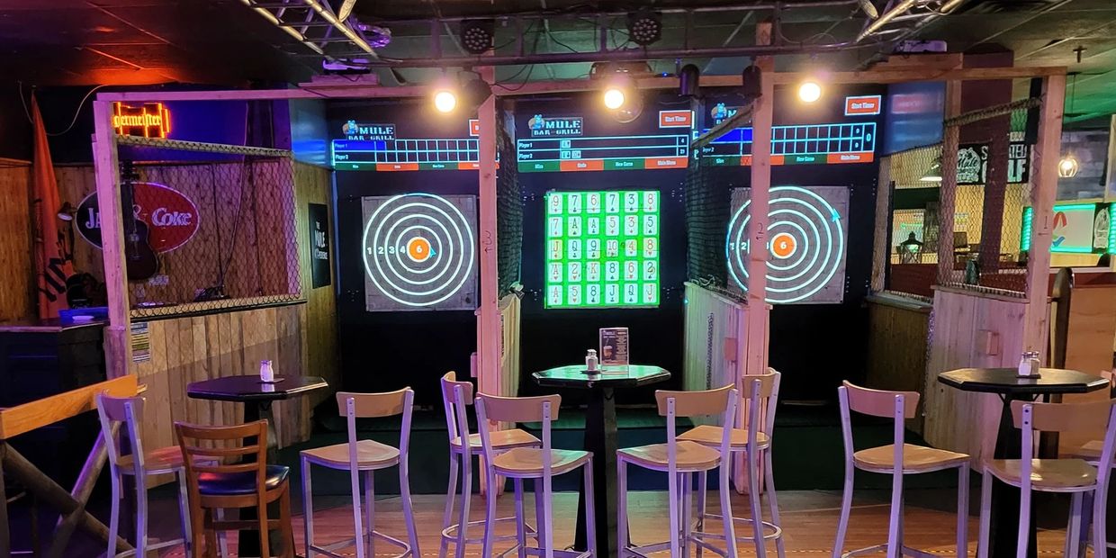 Indoor bar area with dartboards, tables, and chairs under warm lighting.