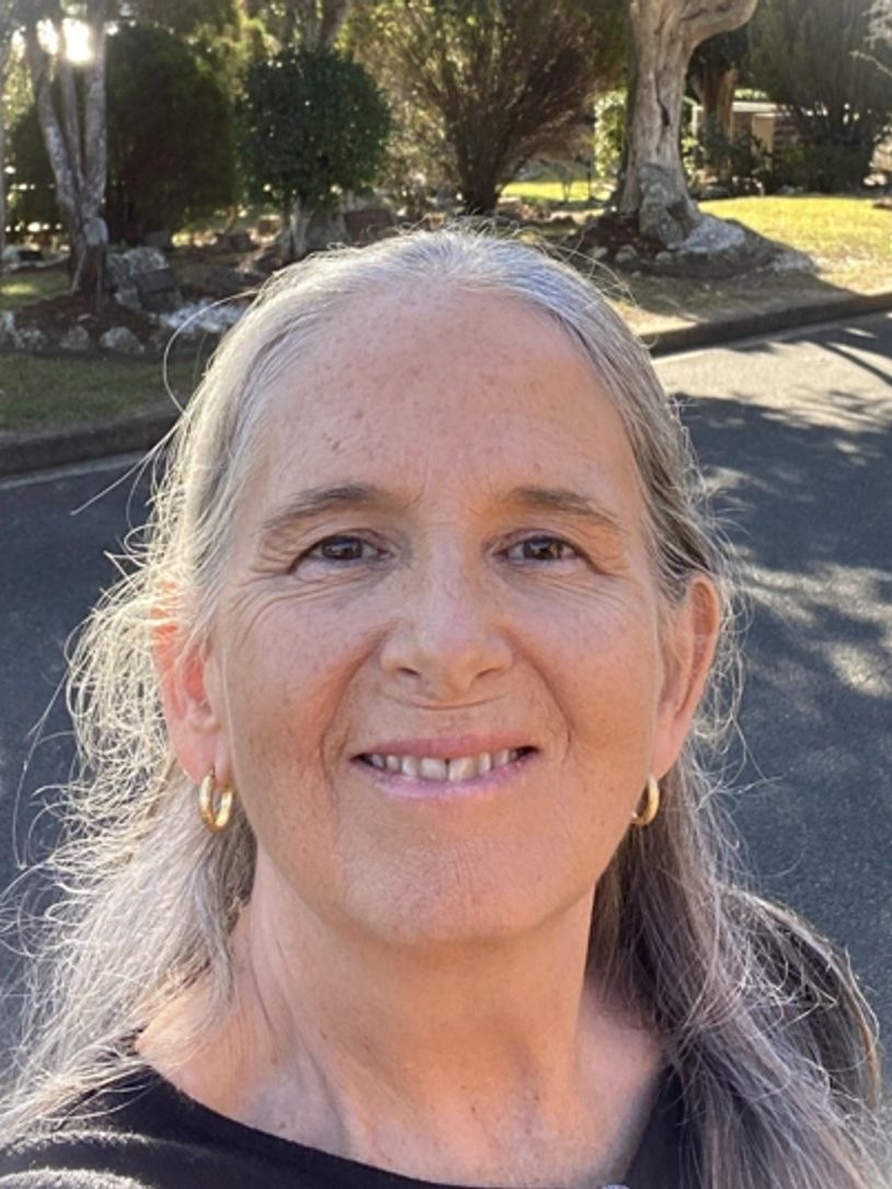Smiling woman outdoors with gray hair and gold hoop earrings.